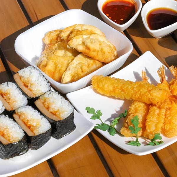 Poki Yaki's fried dumplings, tempura shrimp, and Spam musubi on a wooden table with dipping sauces.