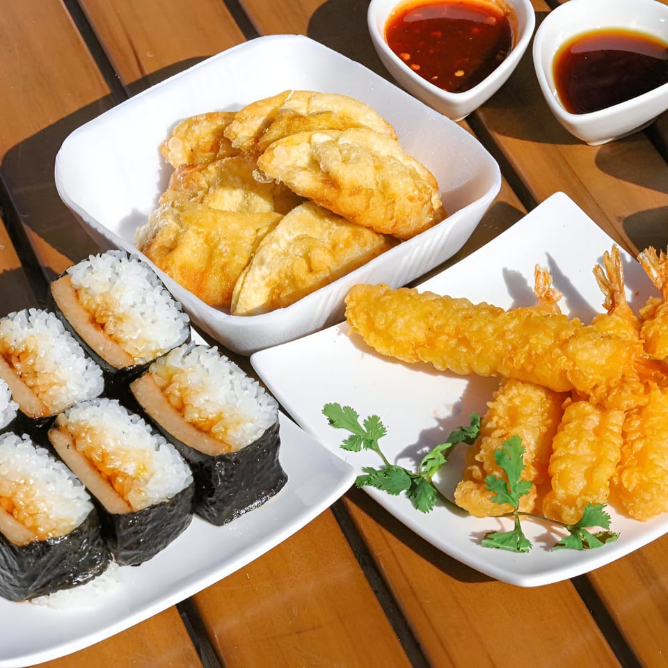Poki Yaki's fried dumplings, tempura shrimp, and Spam musubi on a wooden table with dipping sauces.