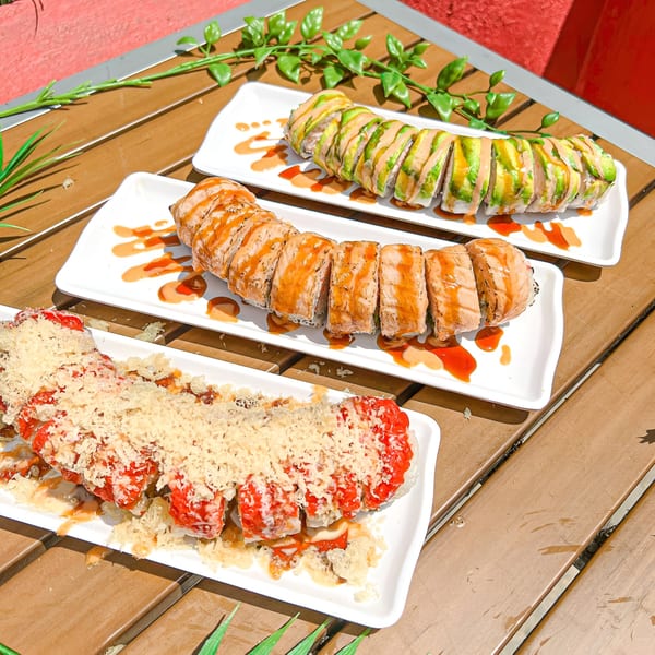 Three plates of colorful sushi rolls with various toppings and sauces on a wooden table.